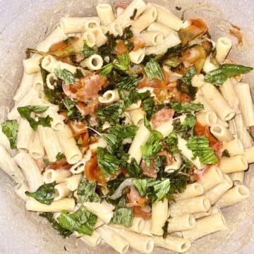 Vegan pasta salad with cherry tomatoes, basil, and fresh greens in a mixing bowl.