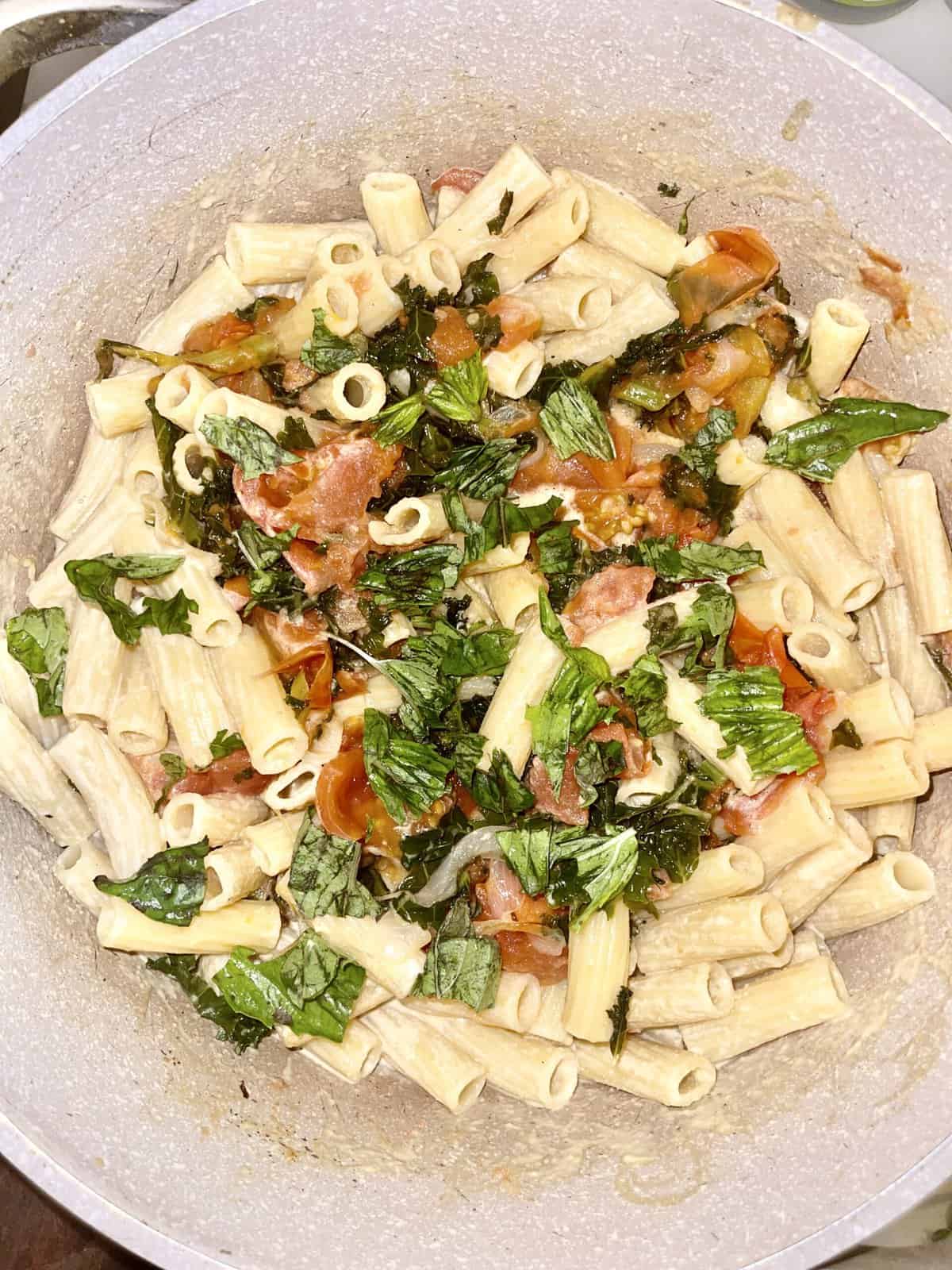 Vegan pasta salad with cherry tomatoes, basil, and fresh greens in a mixing bowl.