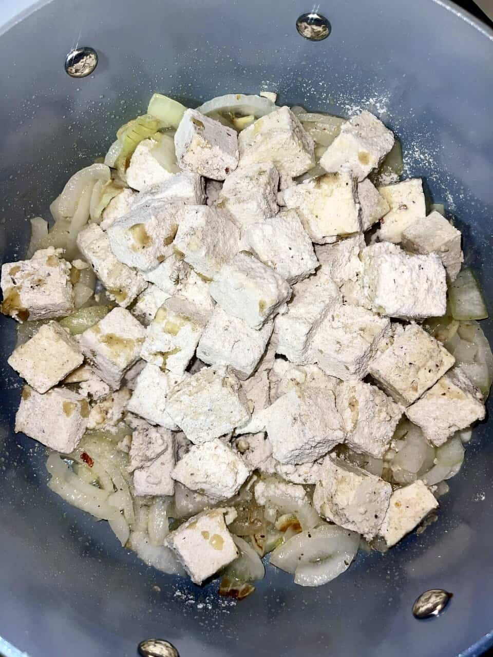 Tofu cooking in a skillet with onions for healthy meal preparation.
