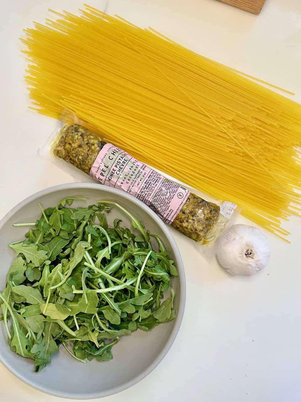 Uncooked spaghetti, fresh arugula, garlic, and a sausage on a white surface for healthy eating.