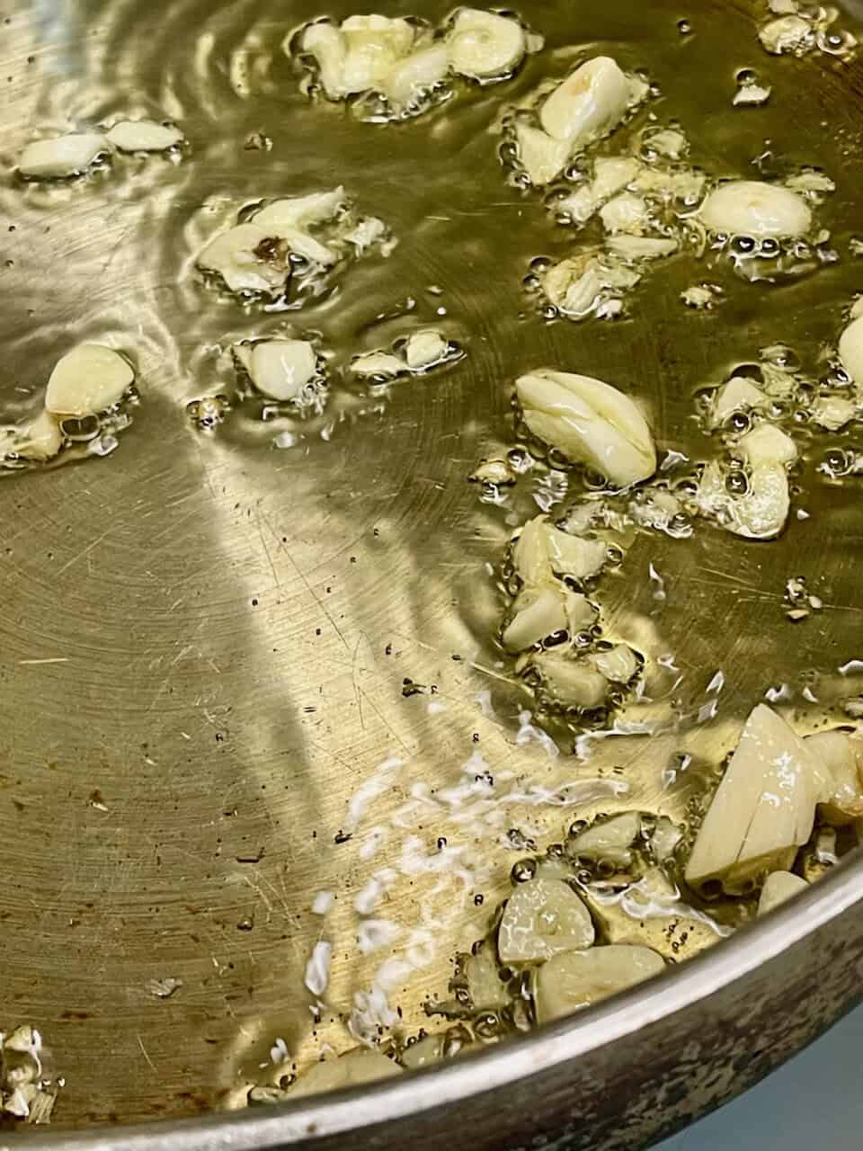 Garlic cloves cooking in a stainless steel pan, aromatic and flavorful ingredient, kitchen cooking, healthy food preparation, culinary basics.