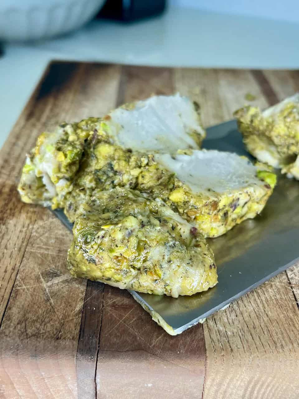 Savory cheese and pistachio wheel with herbs on wooden serving board.