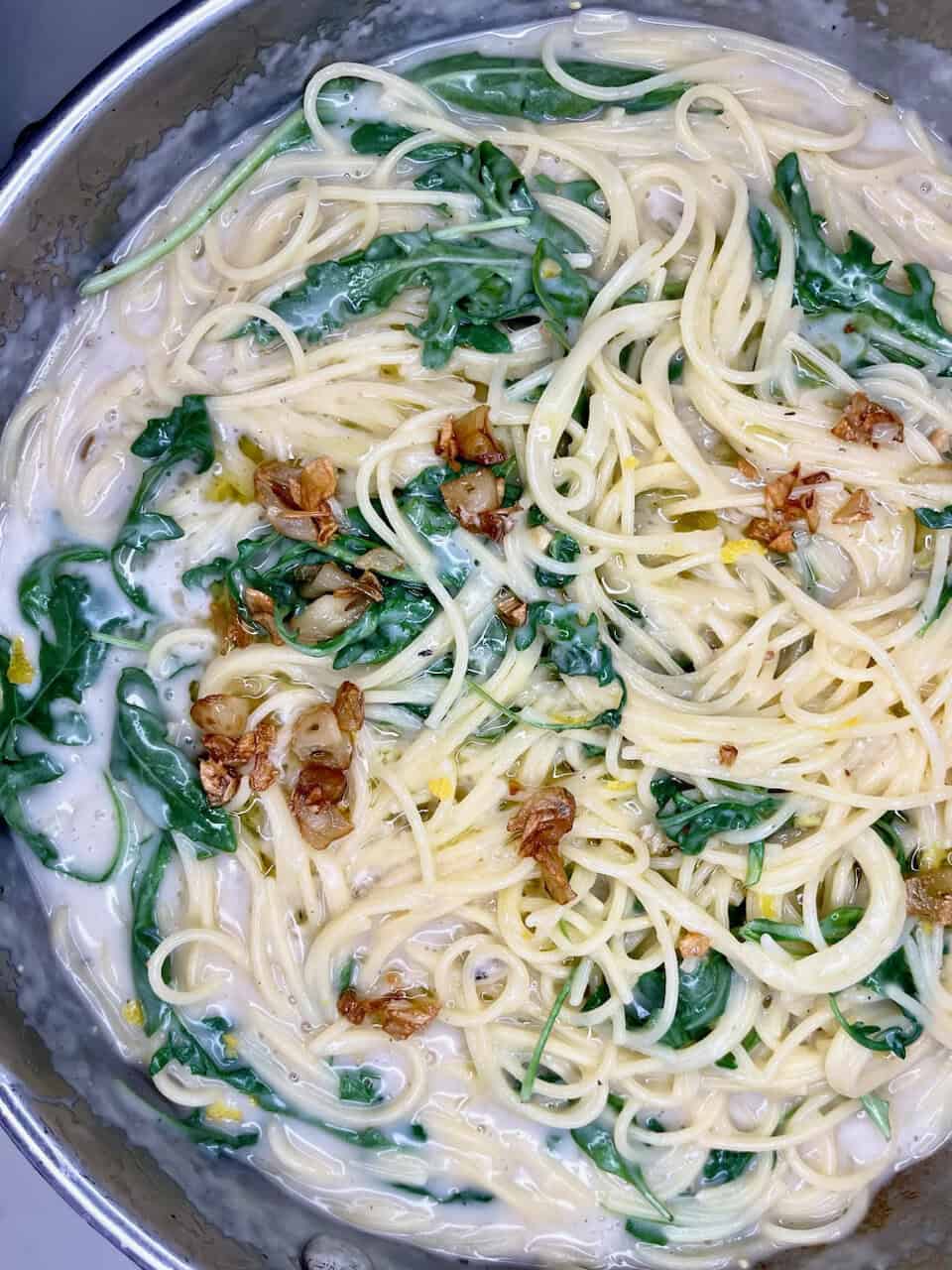 Creamy pasta with spinach and caramelized garlic in a skillet.