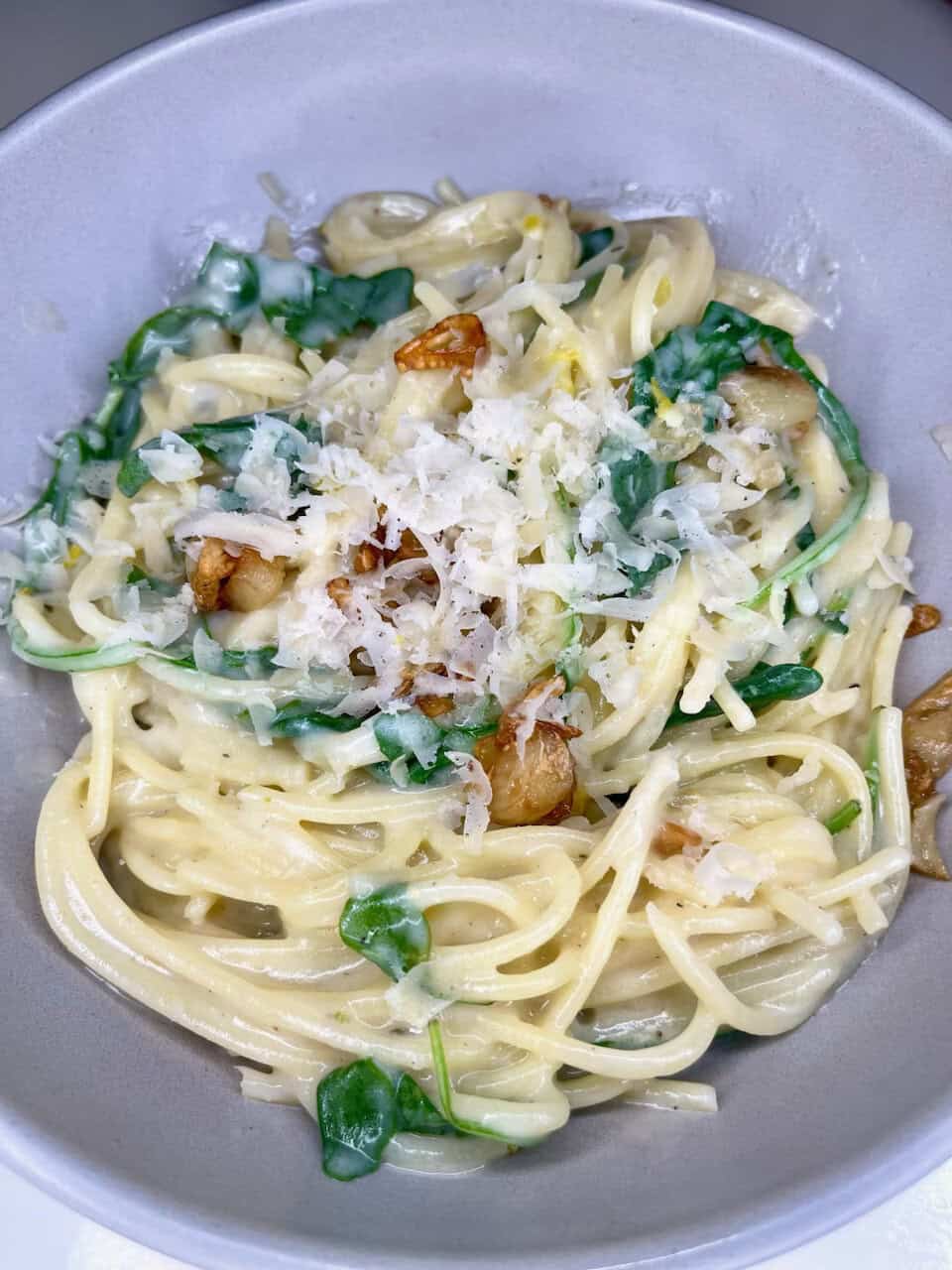 Creamy pasta with spinach, garlic, grated cheese, and toasted garlic pieces in a silver bowl.