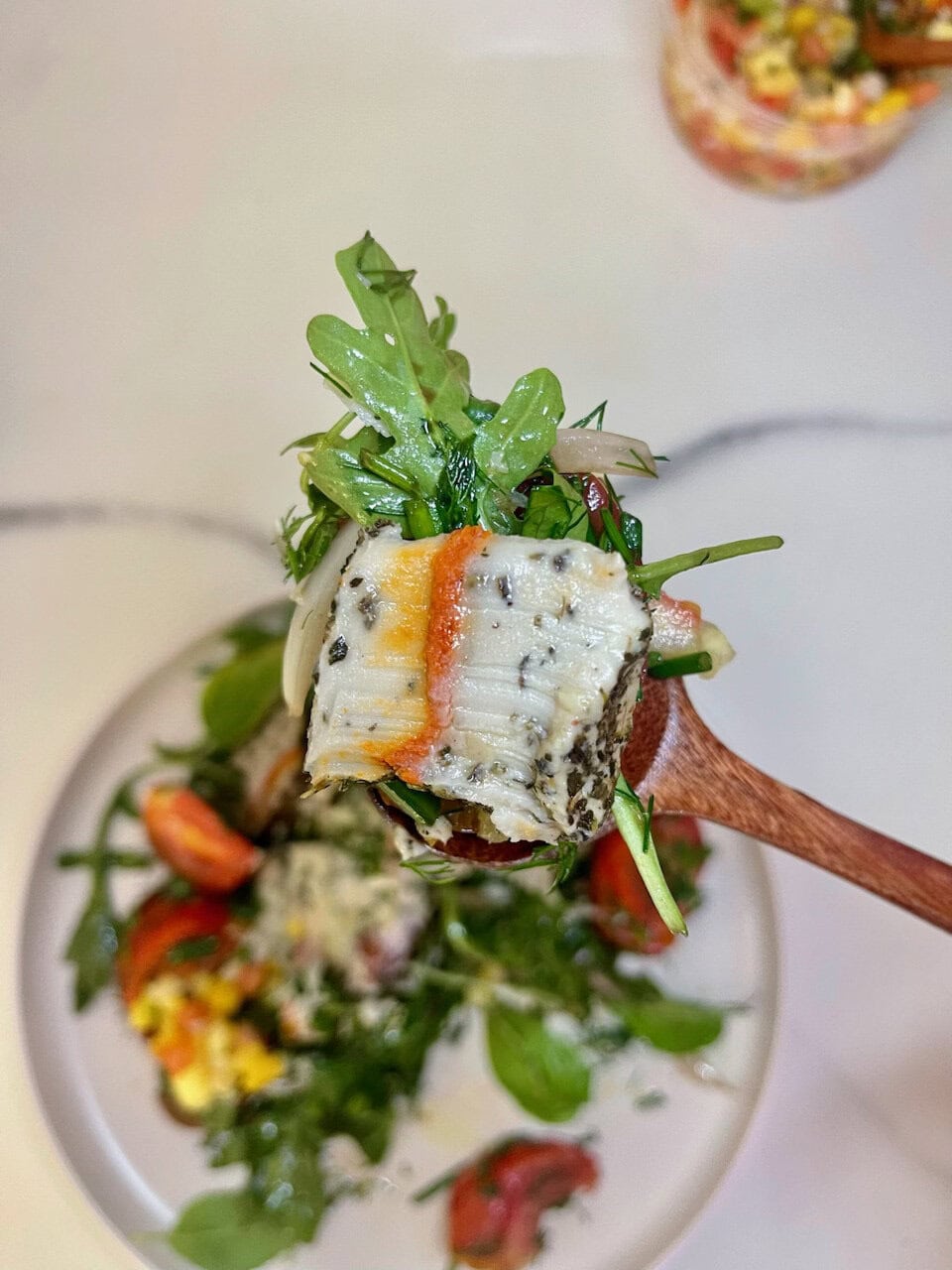 Fresh herb and greens salad with a piece of white fish and vibrant vegetables.