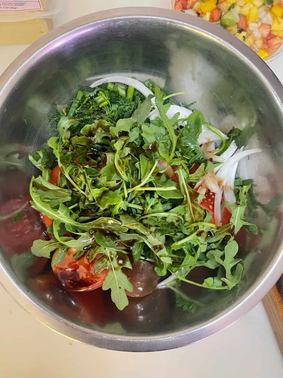 Fresh mixed salad with greens, tomatoes, and vinaigrette in stainless steel bowl.