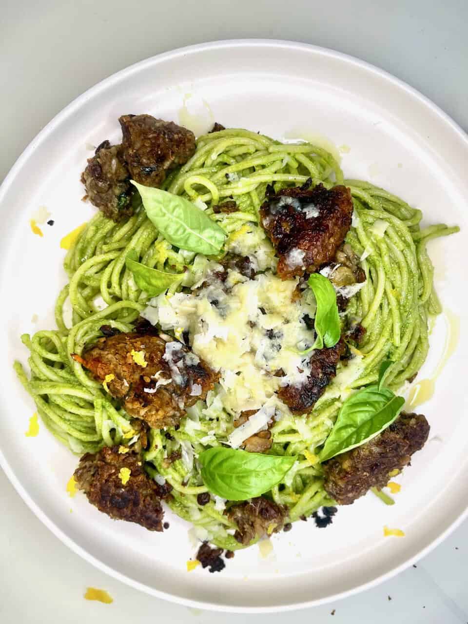 Fresh green pesto spaghetti with grilled meatballs, topped with parmesan cheese and fresh basil leaves.