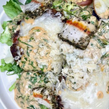 Fresh baked fish with herbs and cheese, served with mixed greens and roasted potatoes, drizzled with creamy dressing.