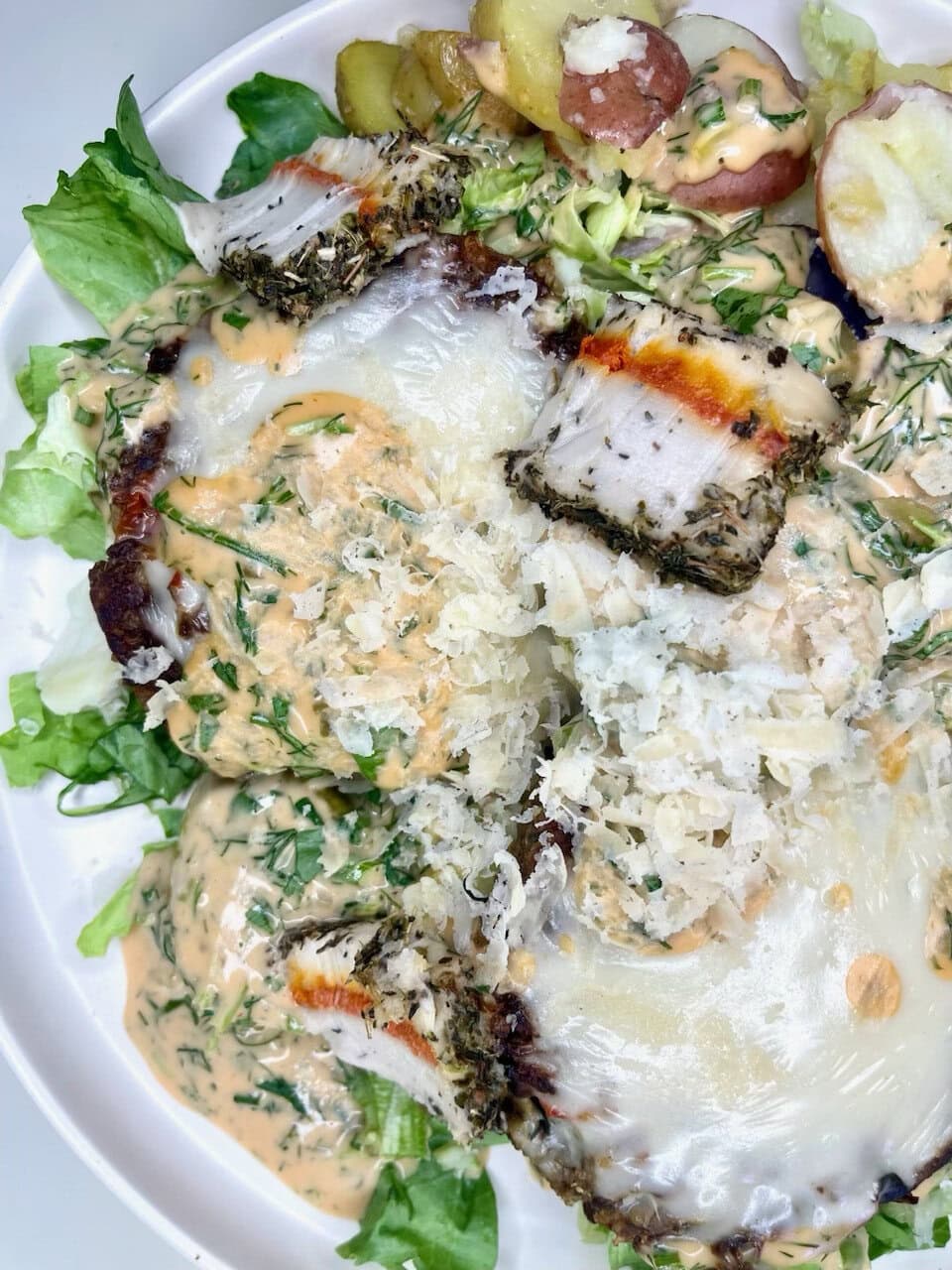 Fresh baked fish with herbs and cheese, served with mixed greens and roasted potatoes, drizzled with creamy dressing.
