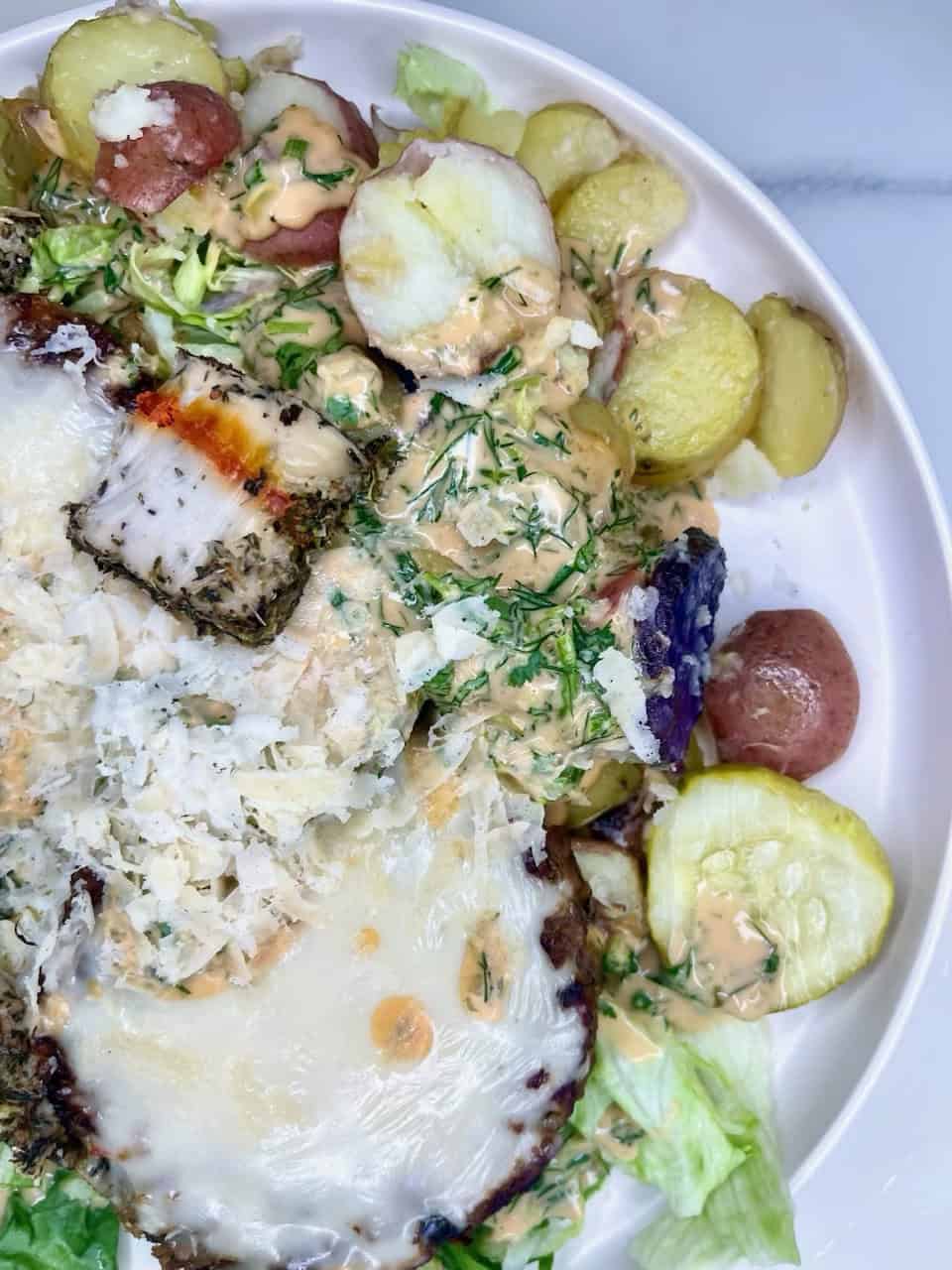 Savory baked fish with herbs and creamy sauce on vegetable salad and roasted potatoes, healthy seafood meal.