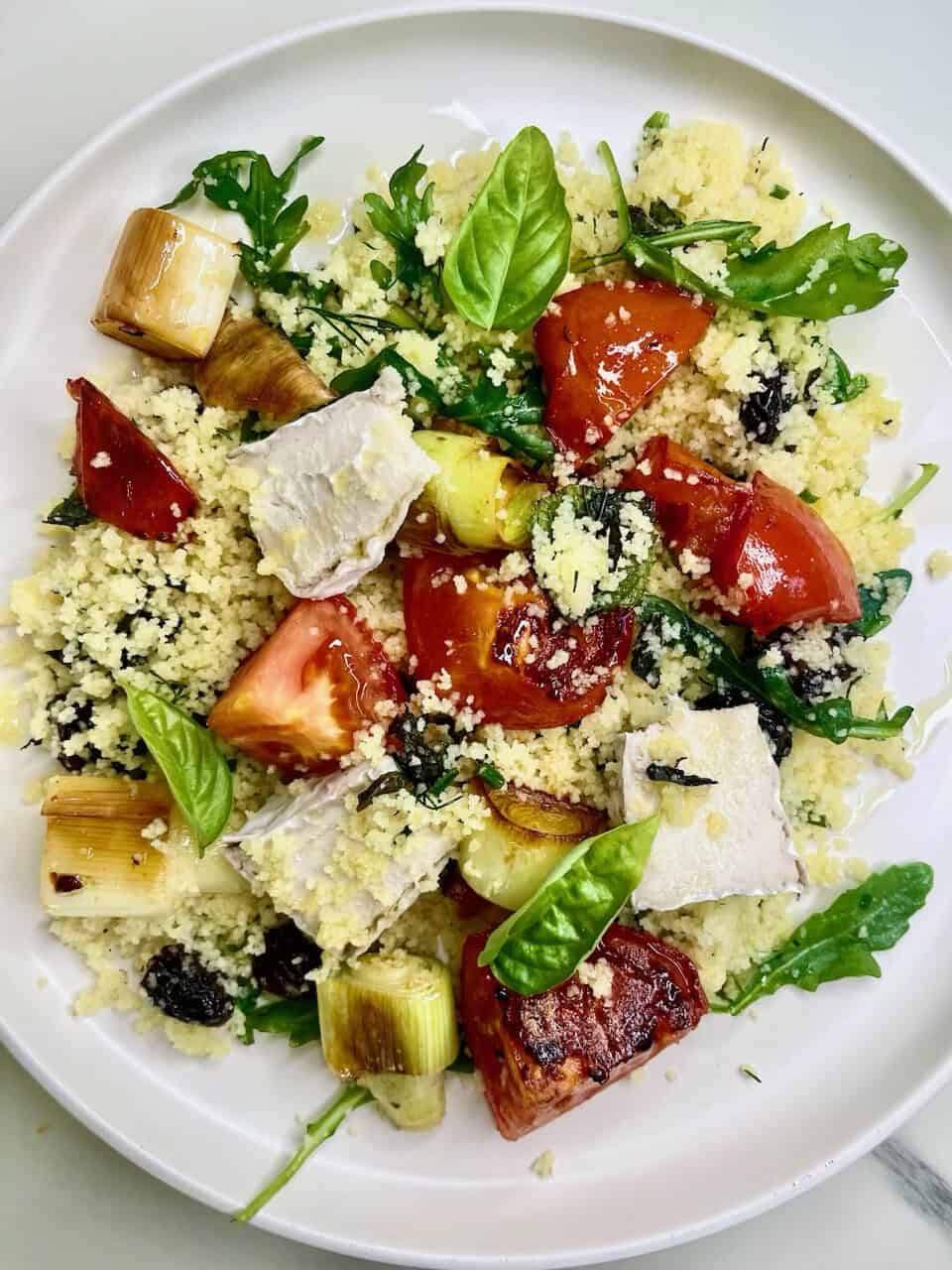 Marinated tomato and vegetable couscous salad with fresh basil and cheese, healthy vegan meal option.
