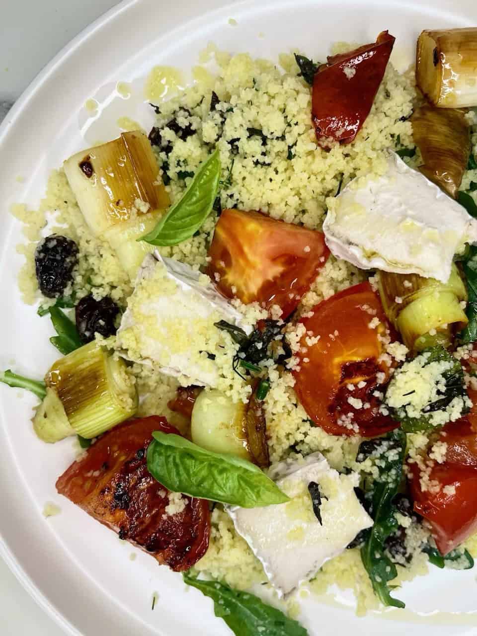 Fresh Mediterranean roasted tomato and vegetable couscous salad with basil, feta cheese, and olives, served on a white plate.