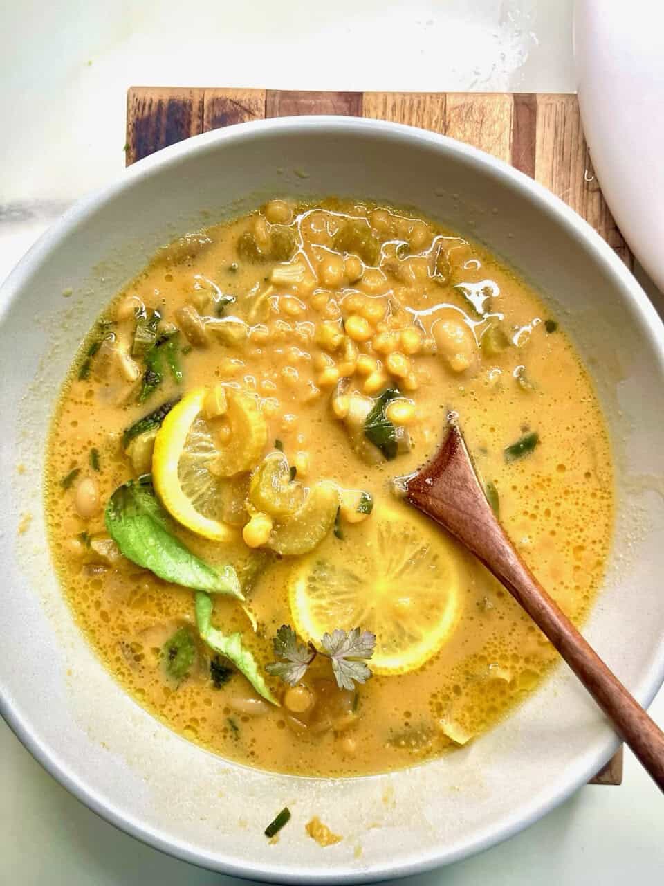 Bright lemon chickpea soup in a white bowl with fresh herbs and slices of lemon for a healthy, nourishing meal.