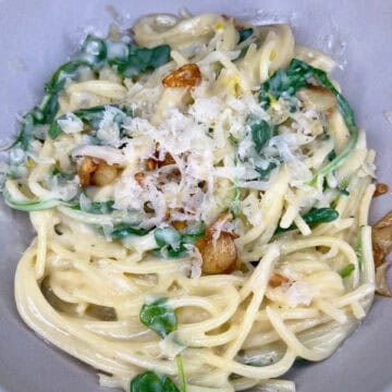 Creamy white pasta with spinach, garlic, and grated cheese in a gray bowl.