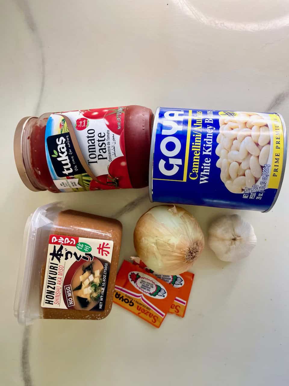 Fresh garlic, onion, tomato paste, canned white kidney beans, and Japanese miso paste for healthy cooking.