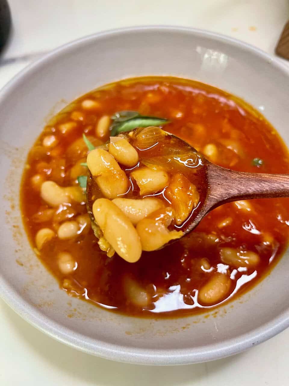 Creamy bean soup with tomato broth and fresh herbs in a white bowl.