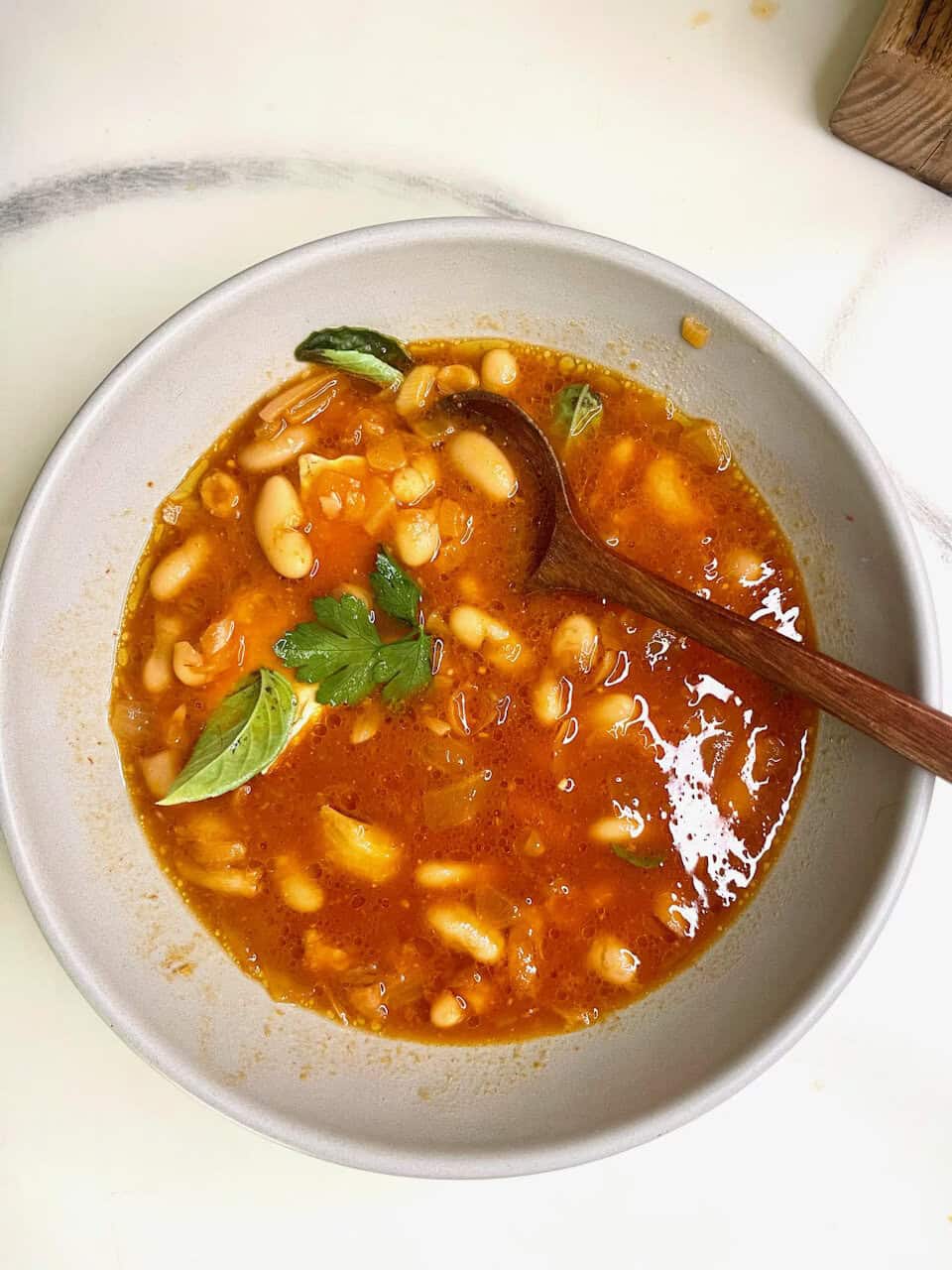 Savory bean soup with fresh herbs in a white bowl.