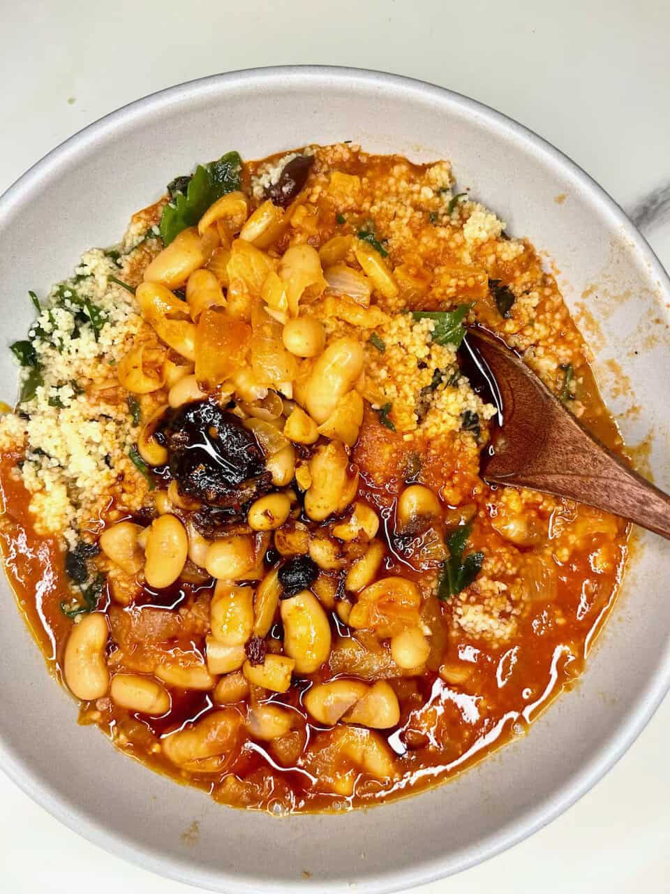 Savory vegan couscous stew with beans, vegetables, and herbs in a white bowl.