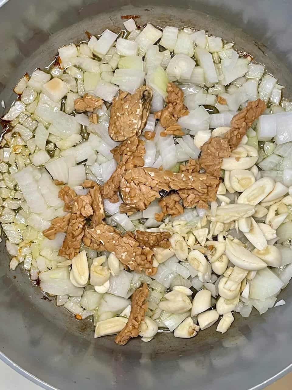 Savory onion and garlic sauté with tempeh in a stainless steel pan, healthy cooking ingredients for vegetarian recipes.