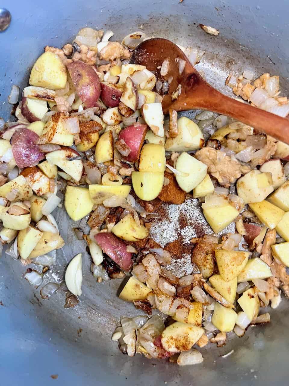 Seasoned diced potatoes and onions cooking in a skillet with a wooden spoon.