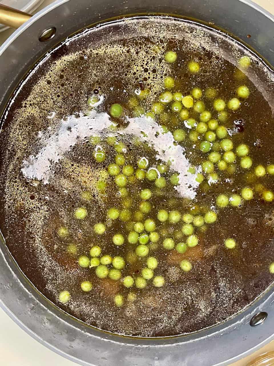 Fresh green peppercorns boiling in water, preparing for herbal or culinary use.