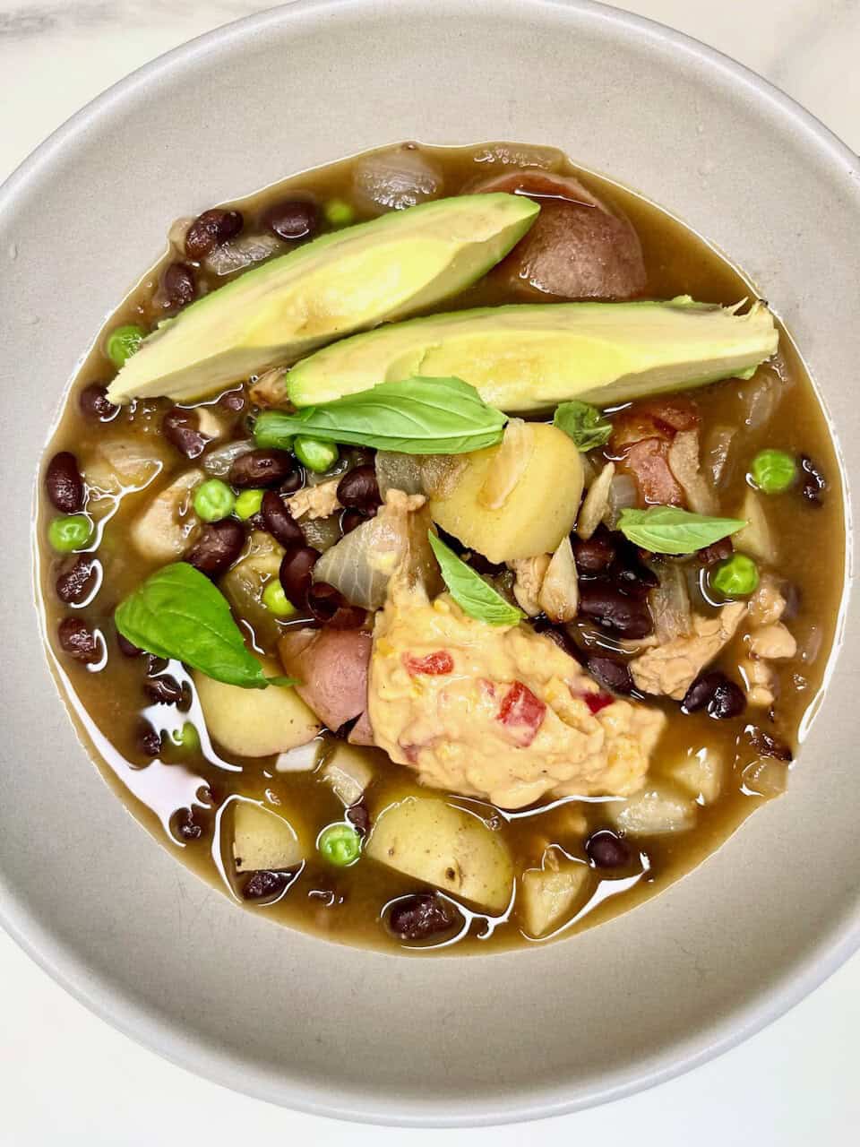 Creamy chicken and black bean soup with avocado and fresh herbs in a white bowl.