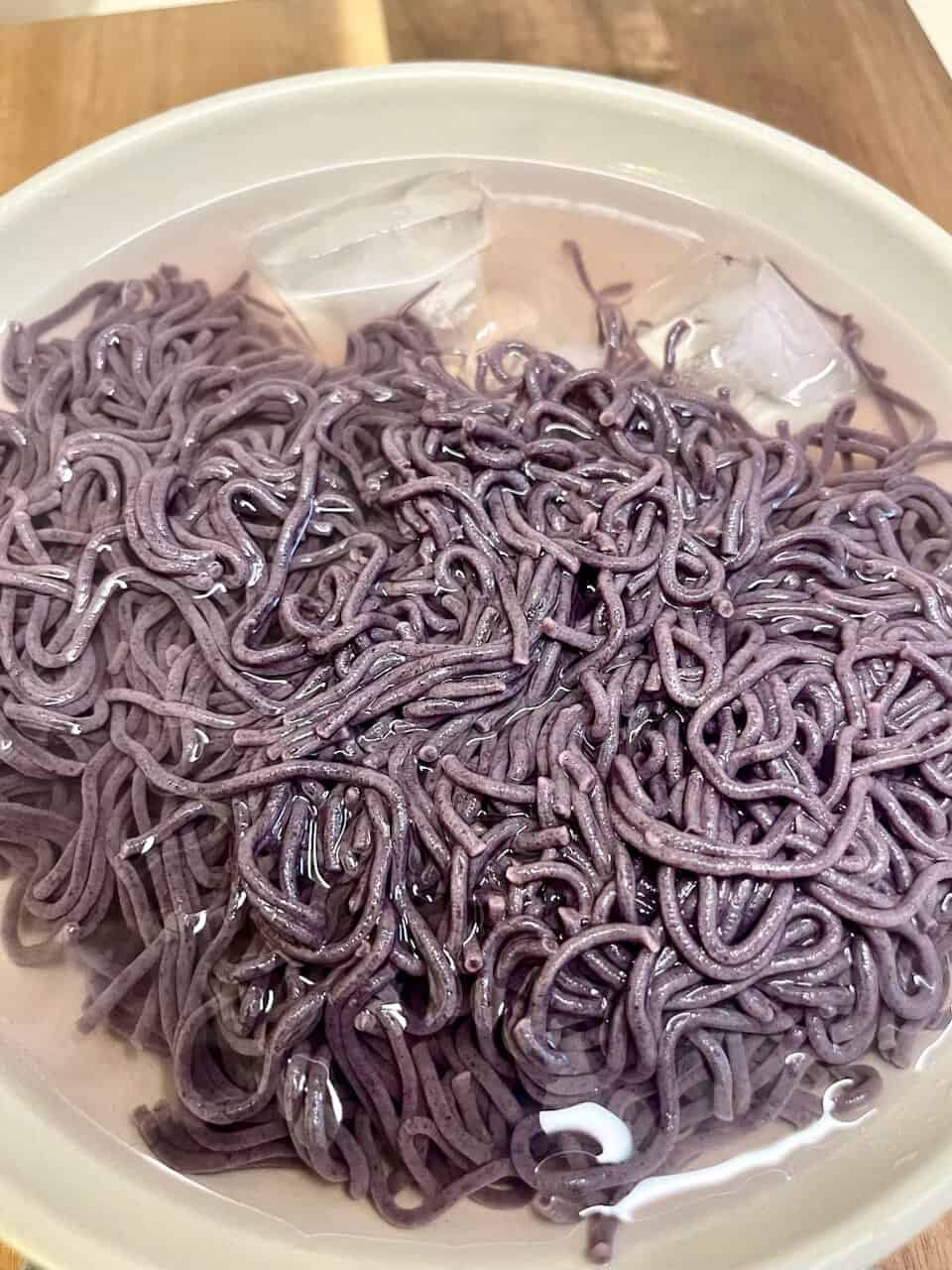 Black sesame soba noodles in a white bowl with ice cubes, healthy and nutritious Asian cuisine.
