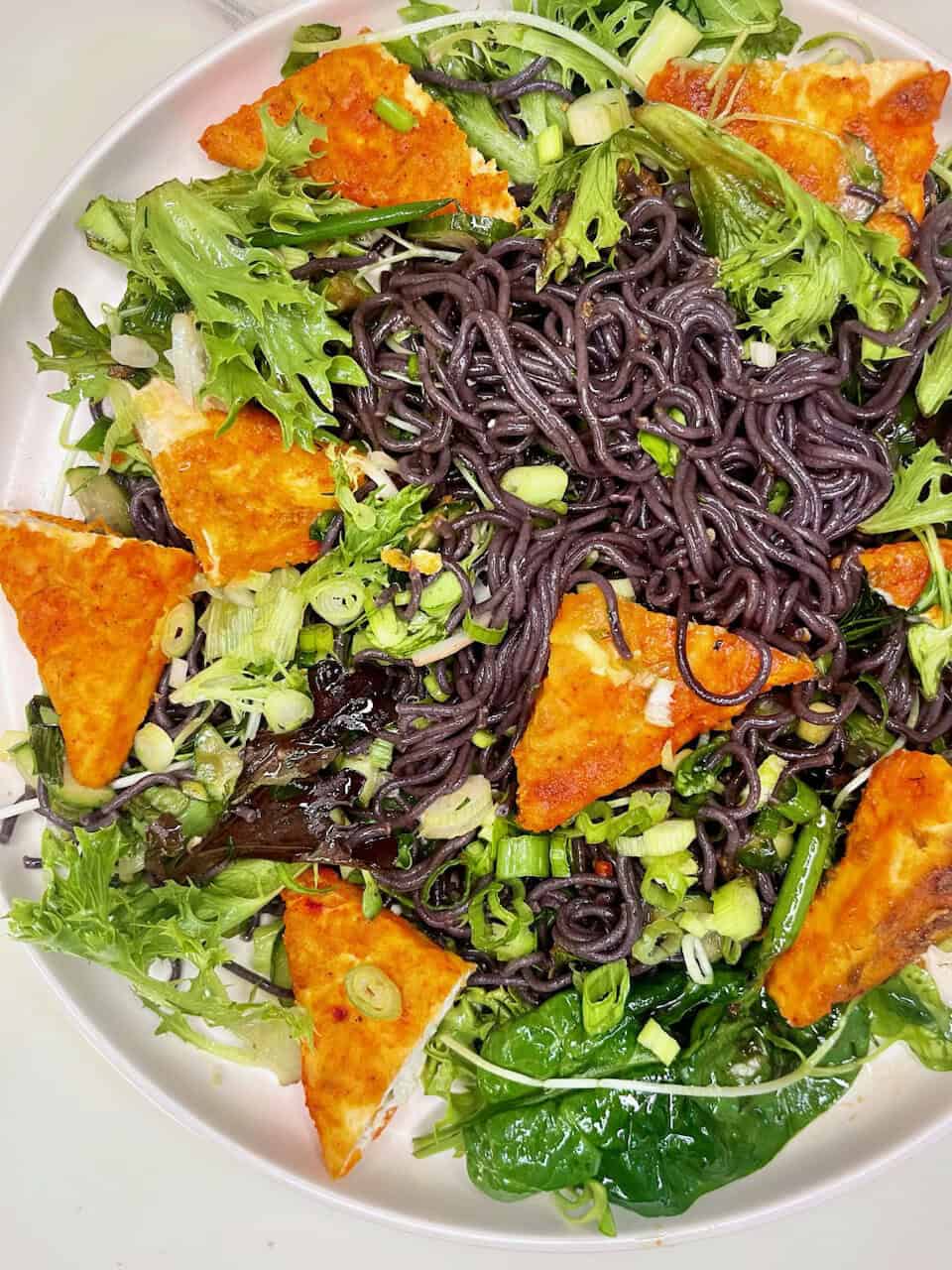 Black charcoal noodles with fresh greens and crispy vegan tofu on a white plate, original healthy recipe from Make Pure Thy Heart.