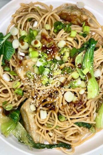 Fresh vegetable Asian noodle stir-fry with green onion, sesame seeds, and soy sauce on white plate.