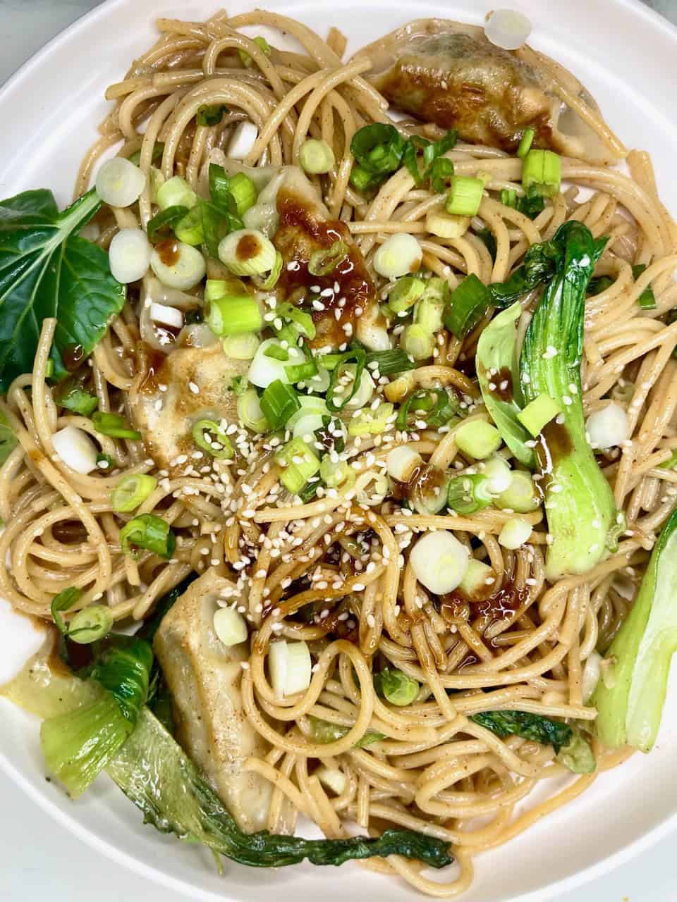 Fresh vegetable Asian noodle stir-fry with green onion, sesame seeds, and soy sauce on white plate.