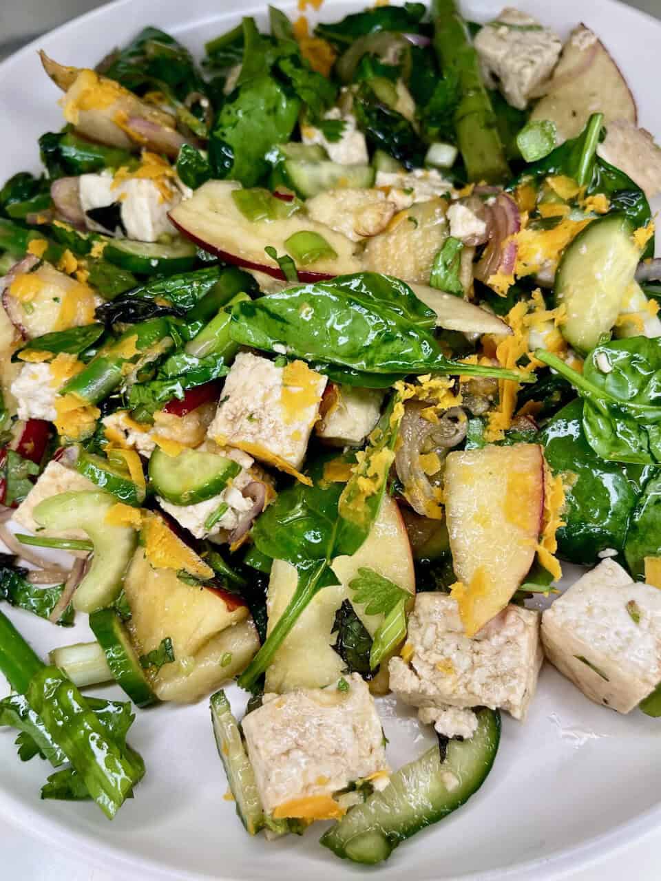 Fresh vegan salad with mixed greens, cucumbers, apples, tofu, and shredded carrots - healthy plant-based meal.