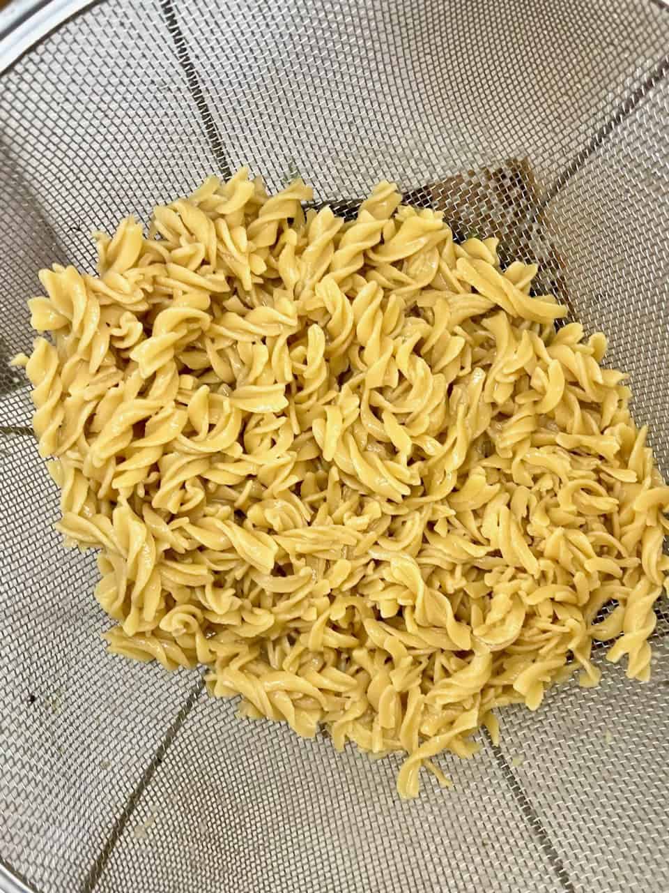 Golden cooked fusilli pasta in a stainless steel strainer, ready for meal prep or cooking recipes.