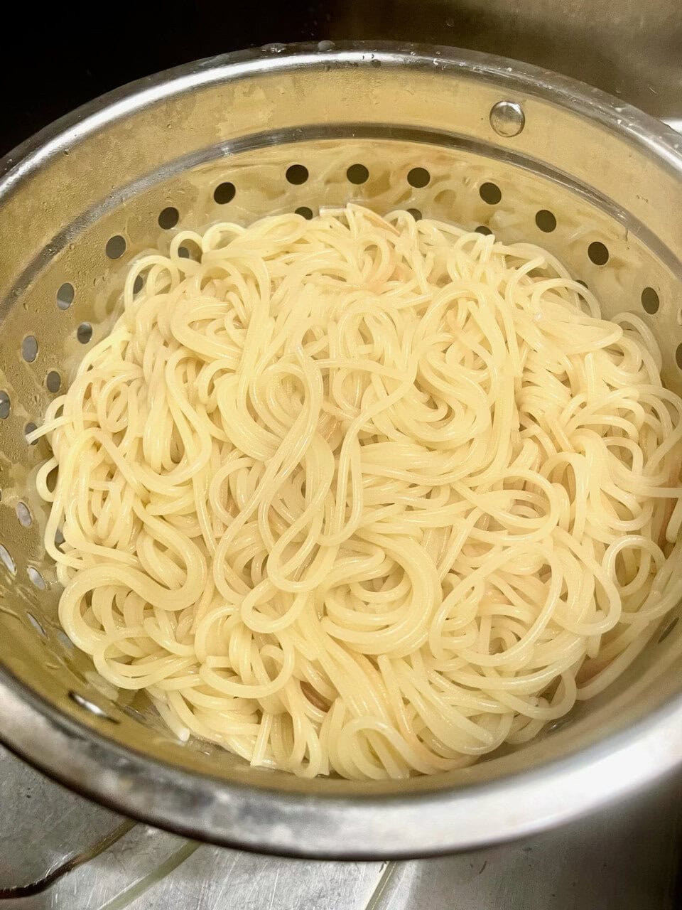 Soft boiled spaghetti noodles in a stainless steel colander.