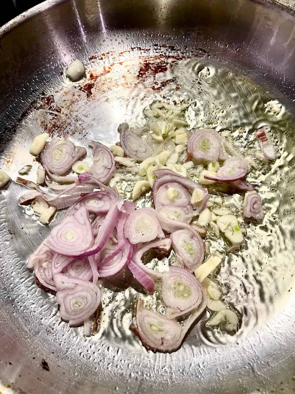 Sautéed red onions and garlic in a stainless steel pan, emphasizing healthy cooking and nourishing ingredients.