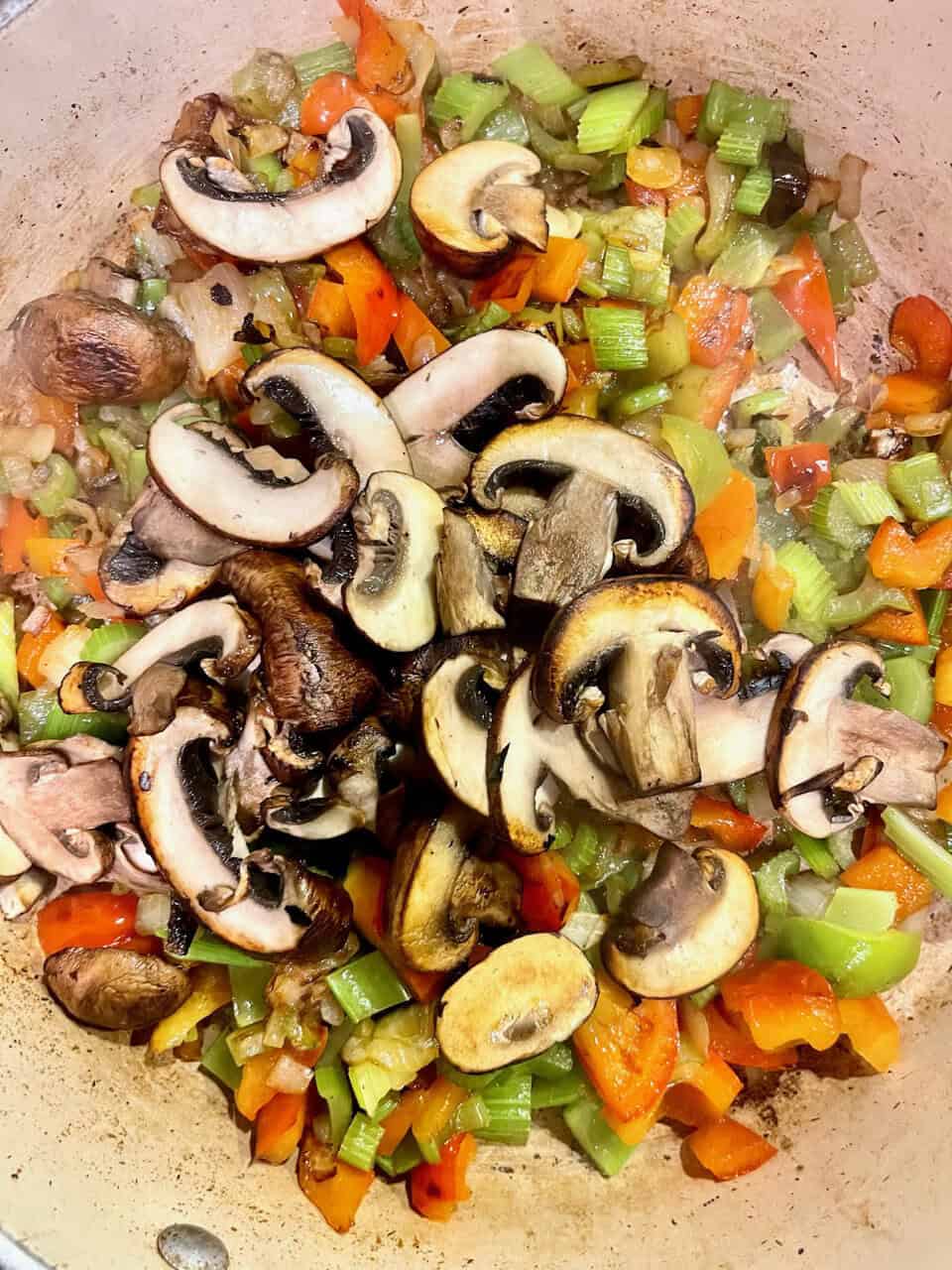 Sauteed vegetables with mushrooms, carrots, celery, and bell peppers in a cast iron skillet.