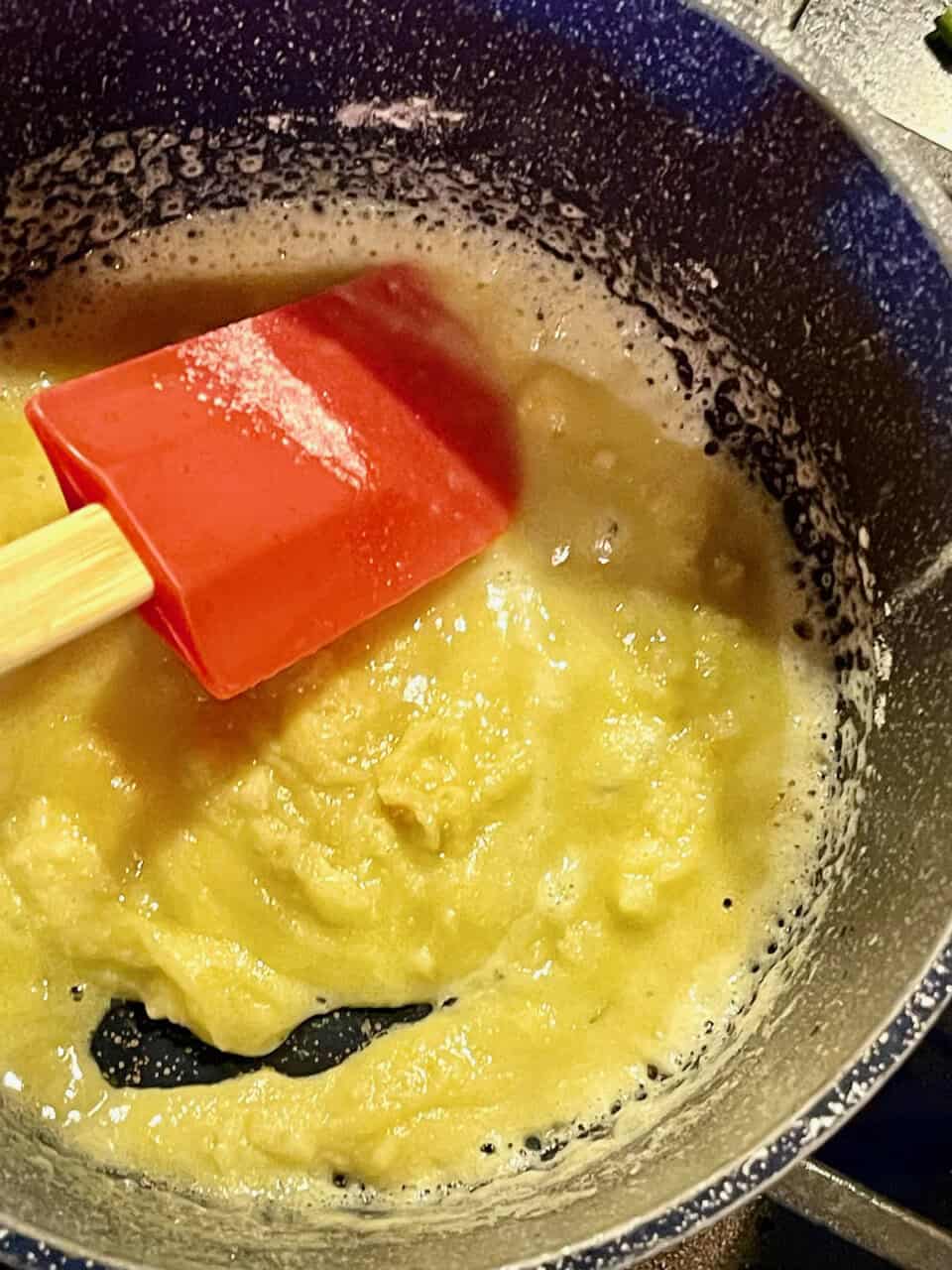 Butter melting in a saucepan with a red spatula stirring it for a homemade recipe.