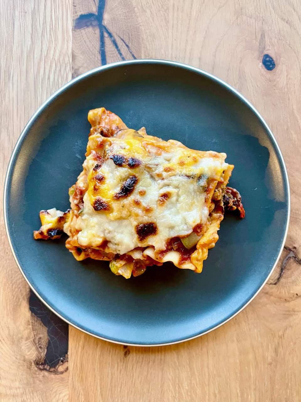 Cheesy vegetable lasagna on a dark plate with a wooden background.