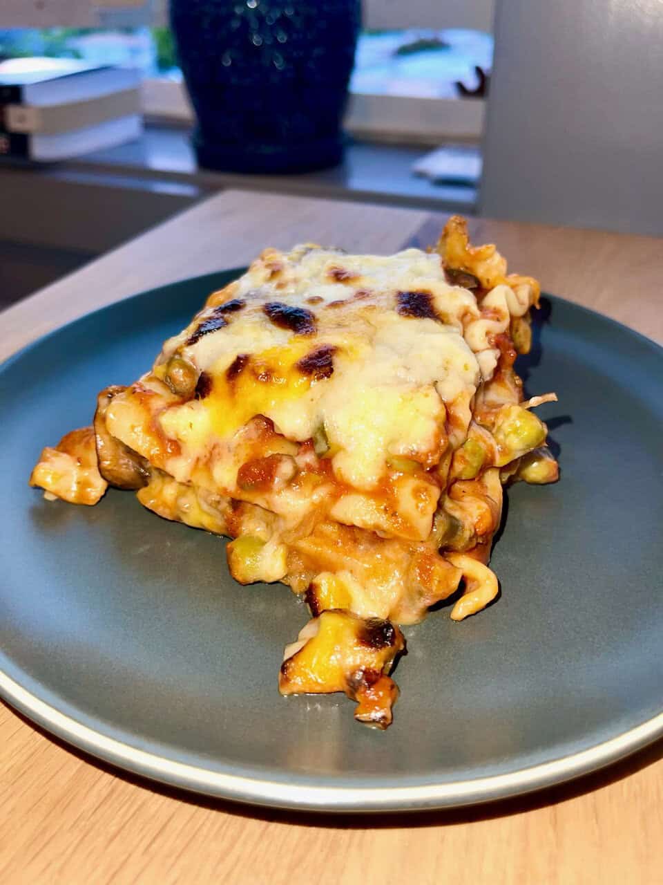 Comfort food baked casserole with melted cheese and vegetables on dark plate.