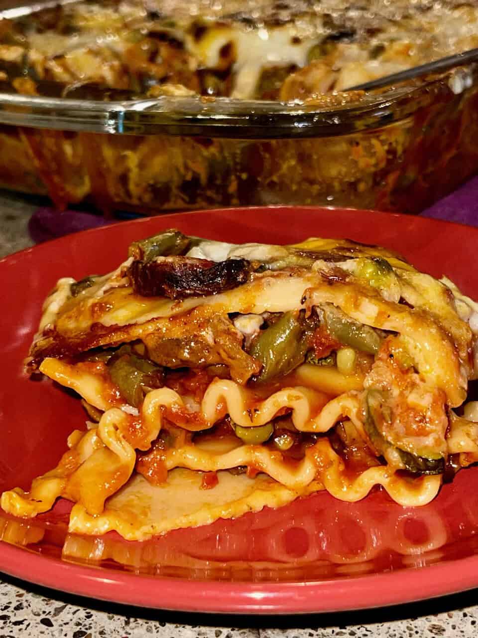 Savory vegetable lasagna with pasta and cheese on a red plate.