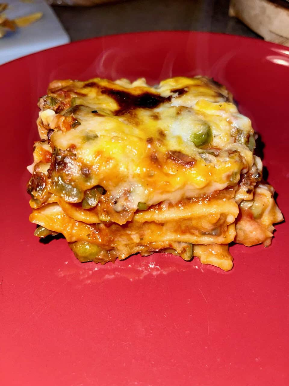 Cheesy vegetable lasagna with melted cheese on top, served on a red plate.