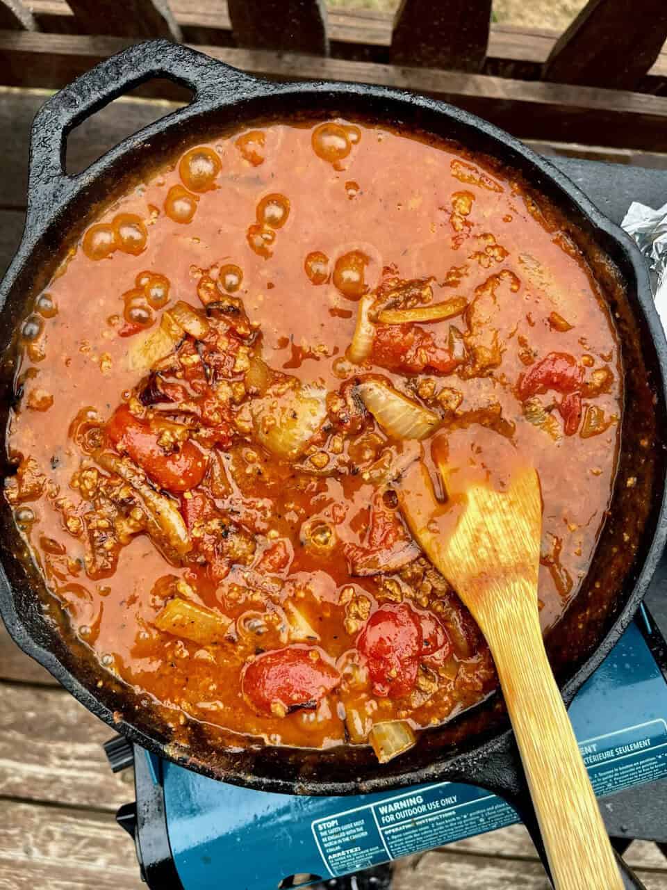 Hearty beef stew cooking in a cast iron skillet with vegetables and rich tomato sauce.