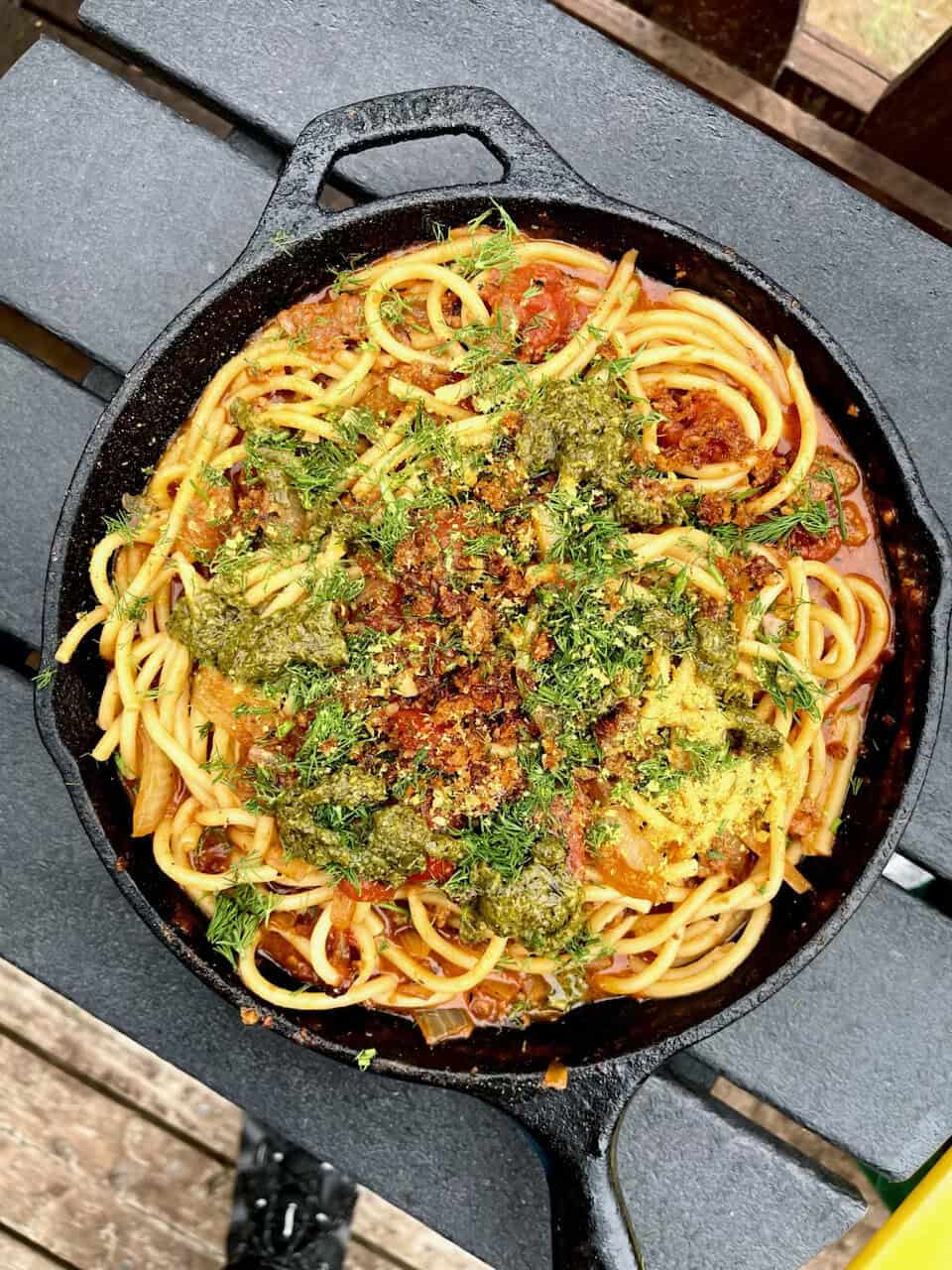 Savory vegan pasta in cast iron skillet with fresh herbs and pesto, healthy plant-based meal for wellness.