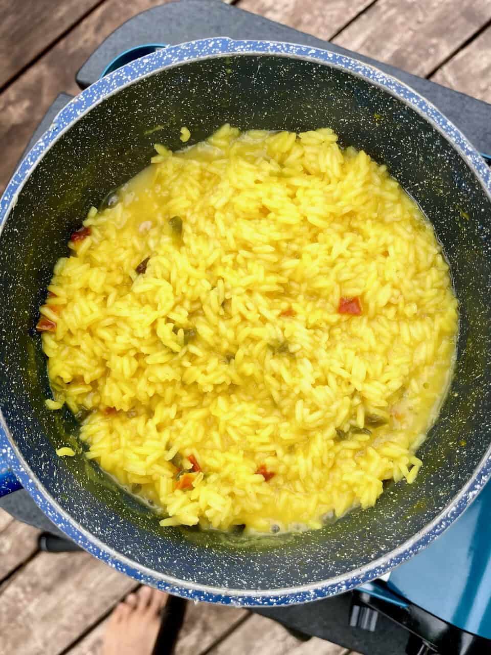 Steamed yellow rice with vegetables in a speckled pot on a wooden deck.