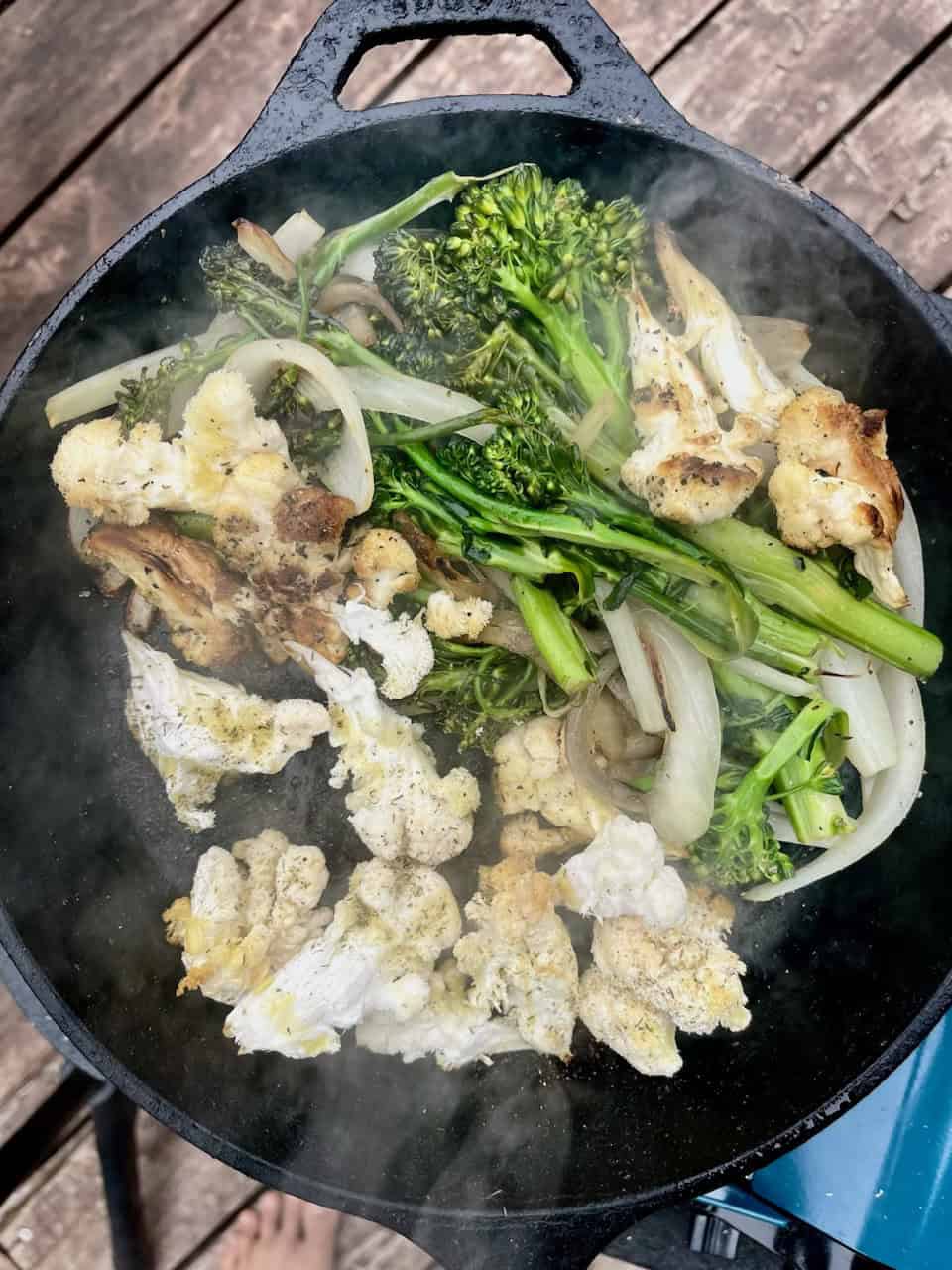 Steamed vegetable medley in a cast iron skillet, featuring broccoli, cauliflower, and onions, emphasizing healthy cooking.