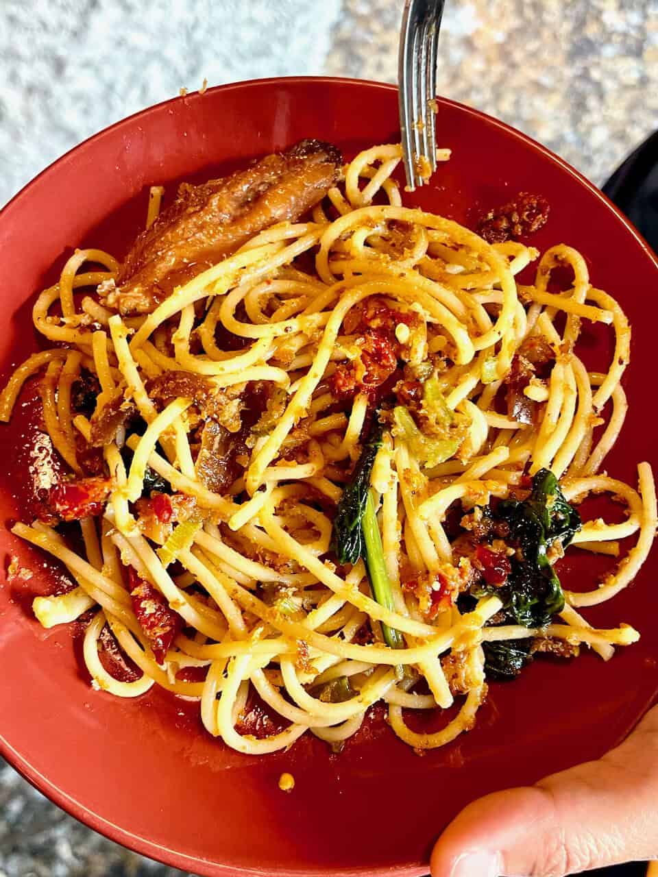 Savory vegetable spaghetti in red bowl with herbs and cherry tomatoes.