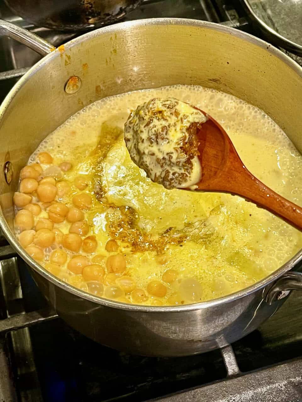 Butter chickpea stew cooking in a pot with a wooden spoon, creamy and hearty, perfect for a nutritious, comforting meal focusing on healthy plant-based recipes.