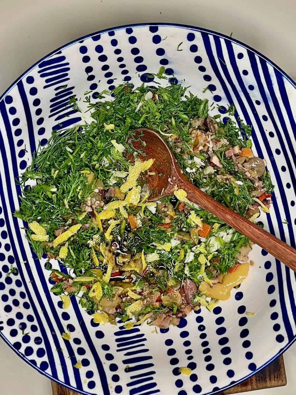 Fresh green herb salad with lemon zest in a decorative blue and white dish, promoting healthy plant-based eating.