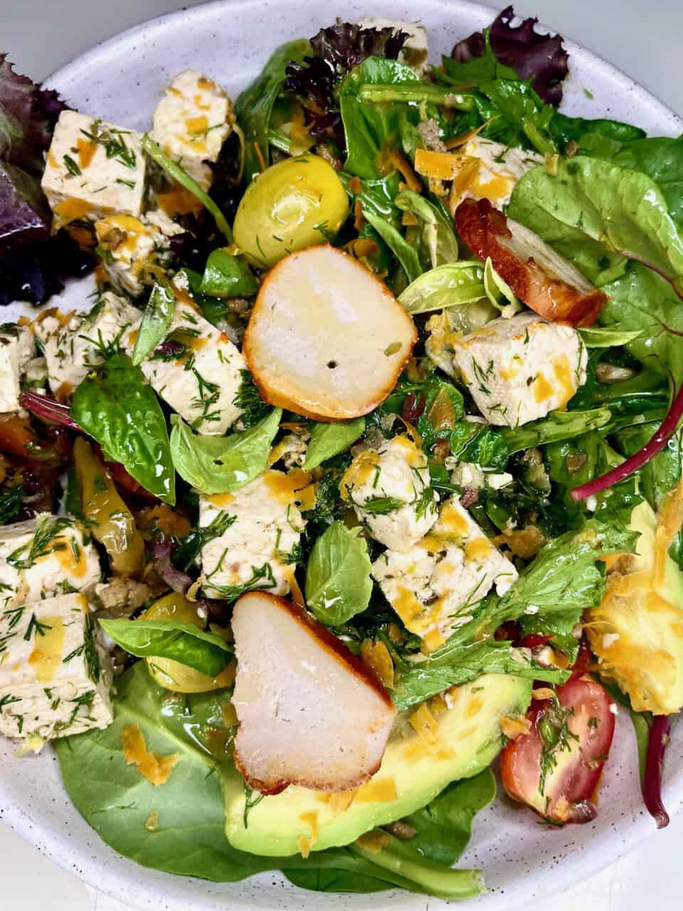 Fresh green salad with tofu, chicken, avocado, and cherry tomatoes, drizzled with a light dressing, promoting healthy living and wellness.