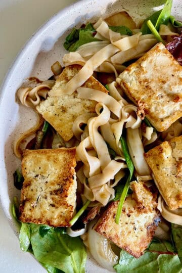 Vegan tofu and vegetable noodle salad with mixed greens and fresh herbs.