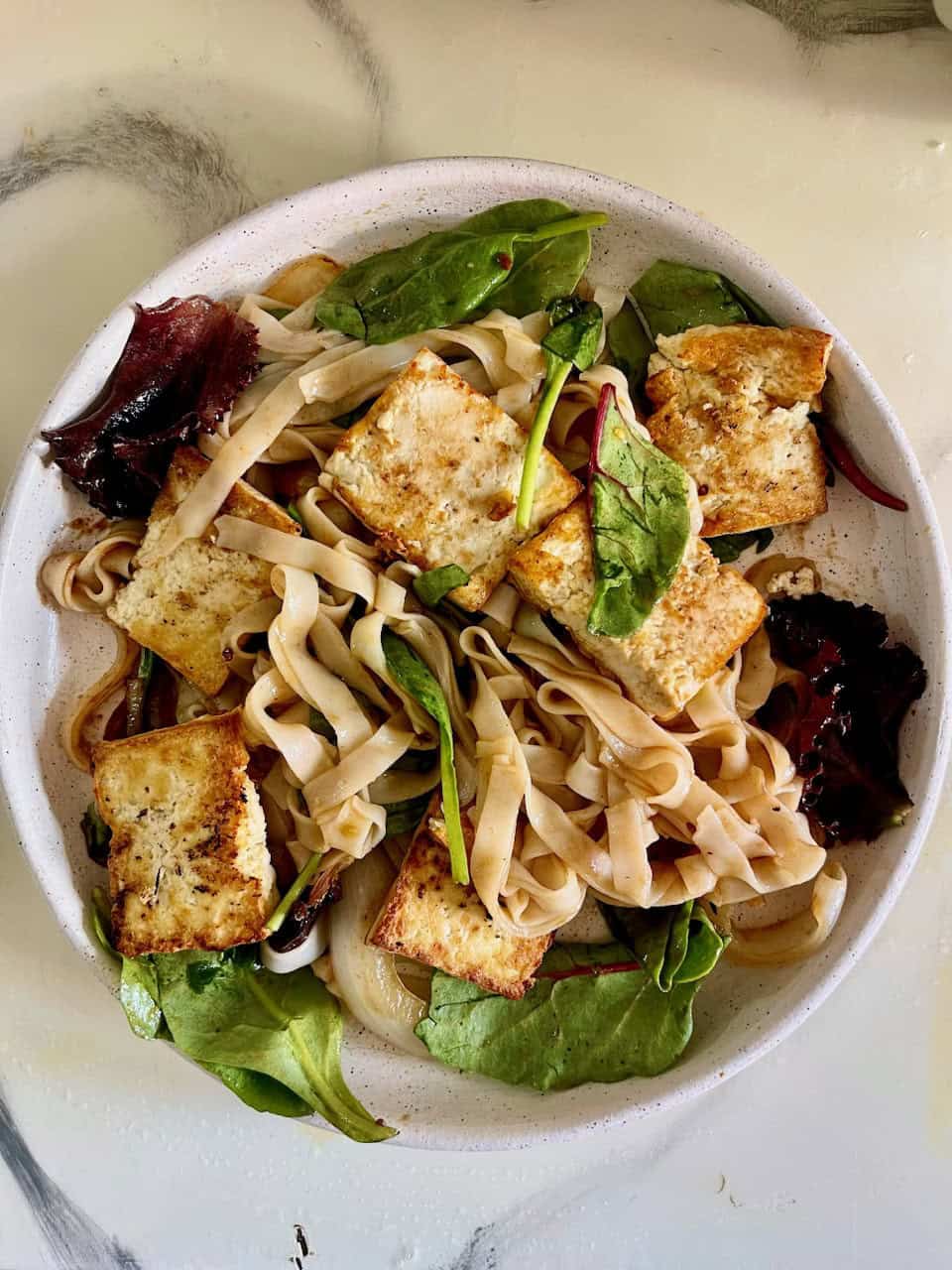 Grilled tofu and vegetable noodle salad with mixed greens, healthy, plant-based meal for health and wellness.